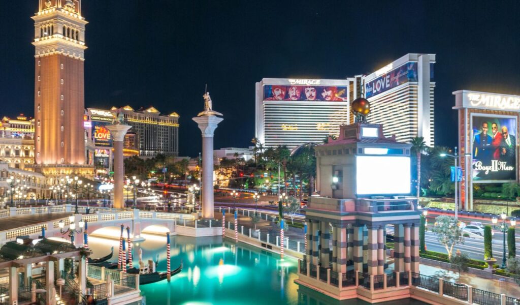 Night view of the Las Vegas Strip with the Venetian Hotel’s canals, gondolas, and illuminated towers, set against a backdrop of neon lights.