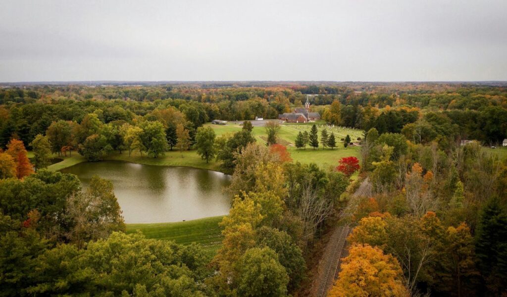 An aerial view of Falls of the Ohio State Park shows a pond, autumn trees, a small church, and a railway cutting through the colorful landscape.