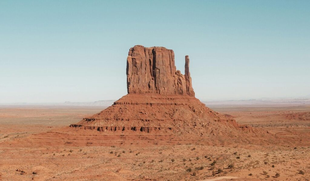 A massive red sandstone butte rises from the flat desert floor at Gold Butte National Monument in Nevada under a clear blue sky.