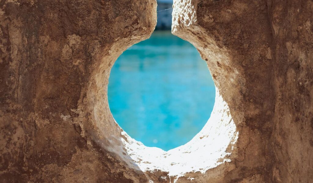 View through a circular rock opening overlooking the turquoise waters of the Great Blue Hole in Belize.