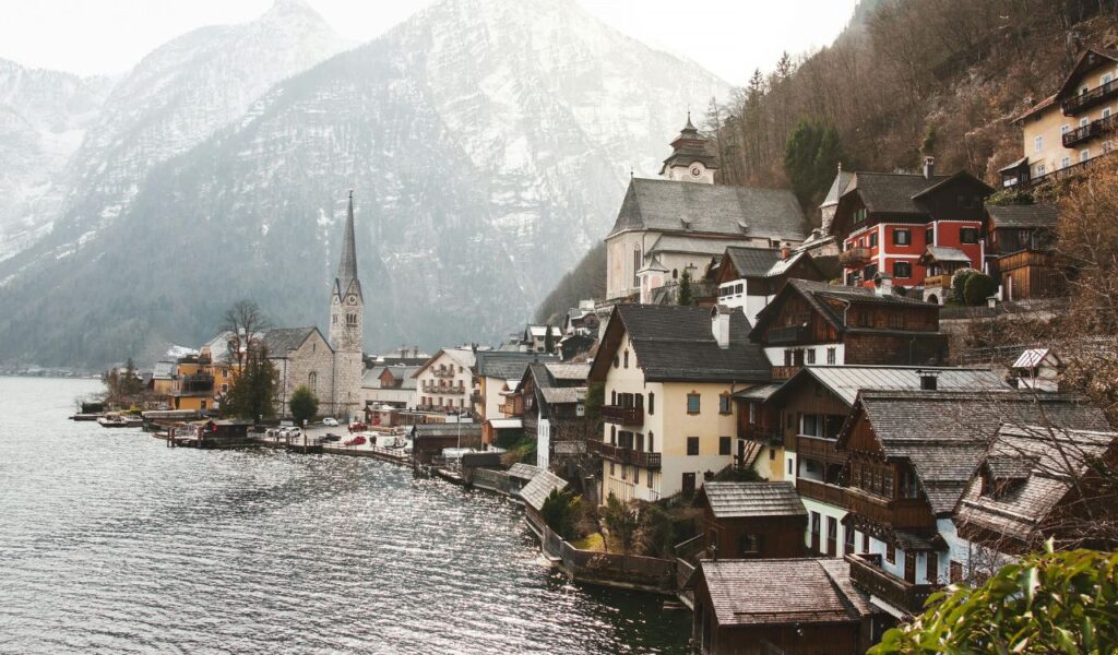Scenic view of Hallstatt, Austria, with alpine houses along the lake, a tall church steeple, and snow-dusted mountains in the background.