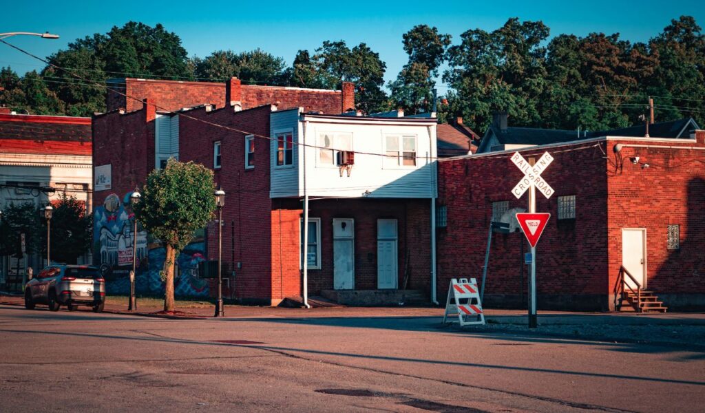 A quiet street corner in Hattiesburg, Mississippi, with red-brick buildings, a railroad crossing sign, a small tree, and warm late-afternoon sunlight.