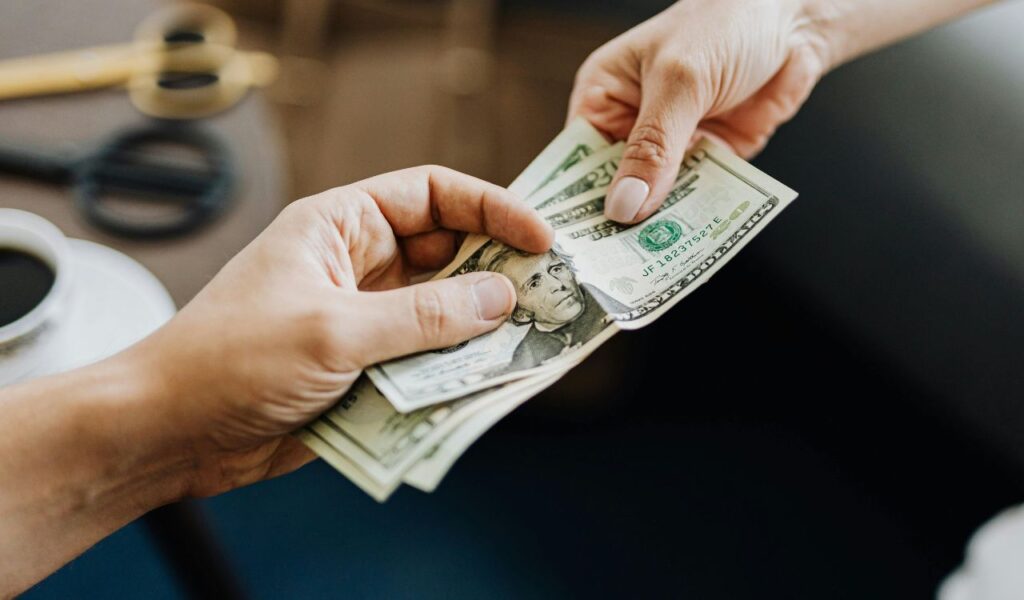 Close-up of one person handing over US dollar bills to another, symbolizing high expenses or payment for goods and services.