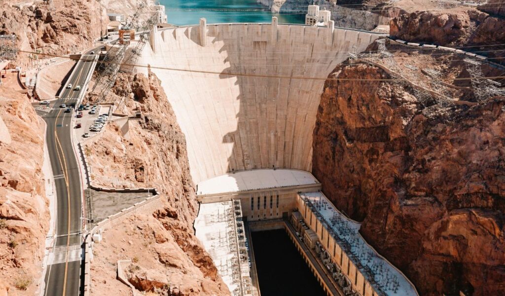 Aerial view of Hoover Dam with its massive curved wall, adjacent roads, and surrounding rocky canyon landscape.