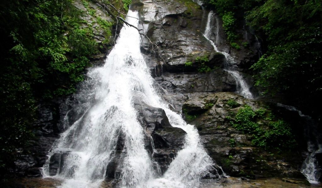 Cascading High Shoals Falls in Georgia, with multiple streams of water tumbling down dark rocky cliffs surrounded by lush greenery.