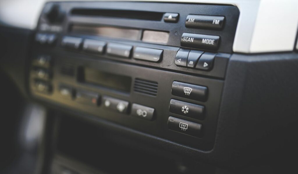 Close-up of a car stereo system showing AM and FM radio buttons, scan and mode controls, and various dashboard buttons.