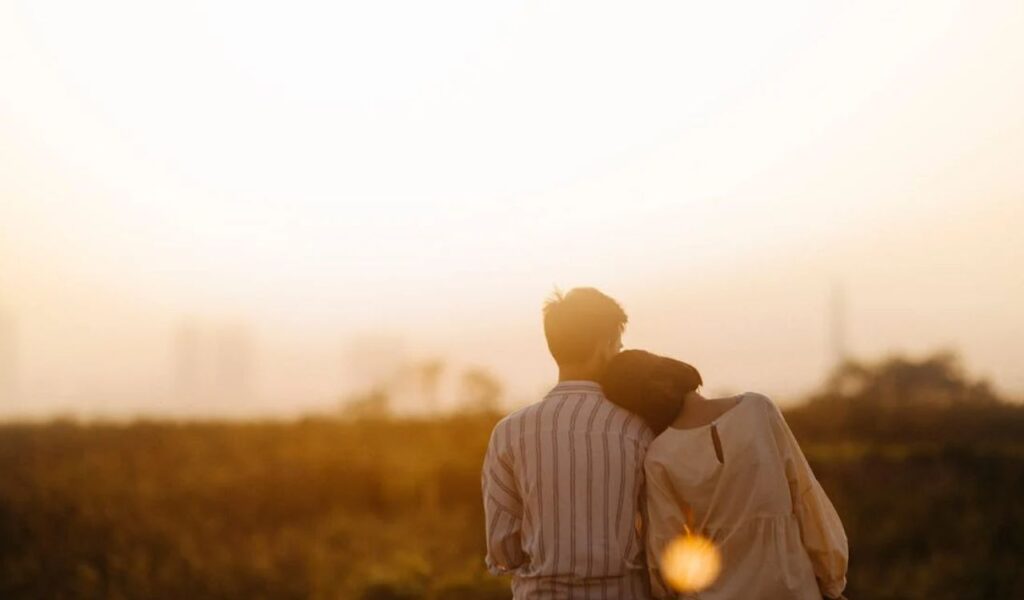 A couple sitting close together surrounded by glowing candles, watching the sunset over a city skyline.