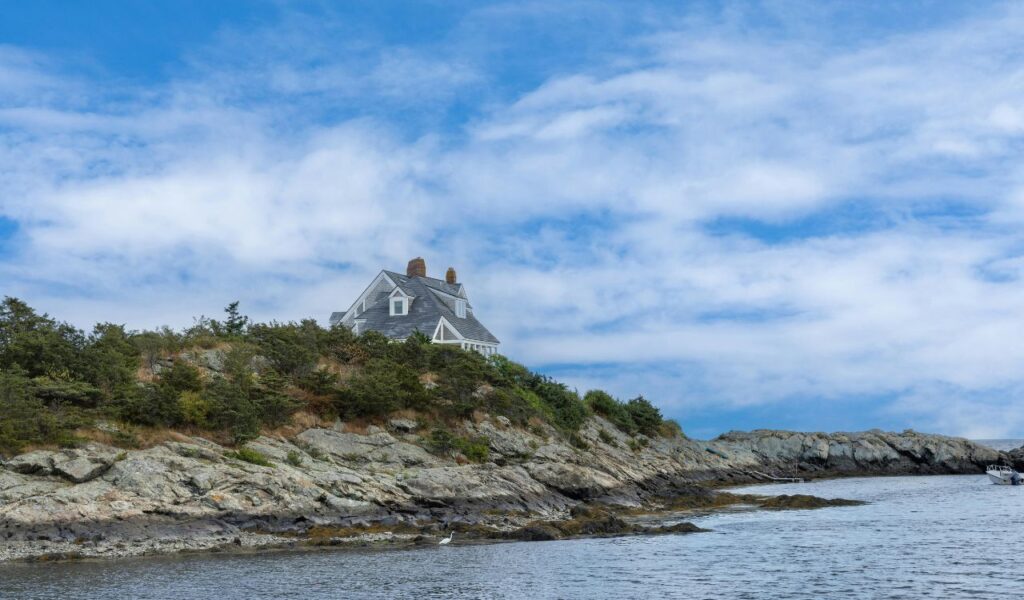 A coastal home sits high on a rocky bluff in Little Compton, Rhode Island, overlooking the ocean and surrounded by windswept greenery and rugged cliffs.