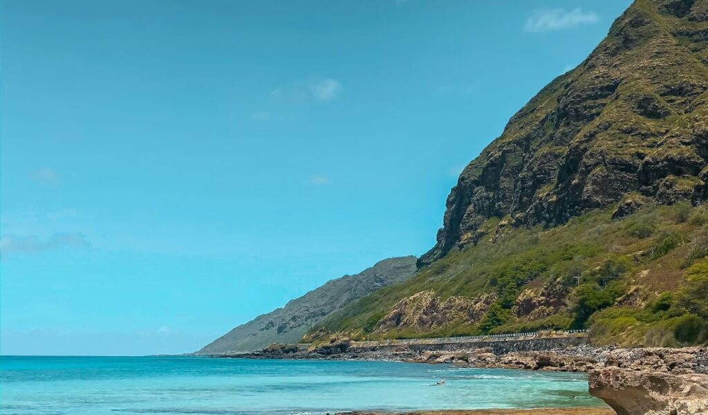 Clear turquoise waters along the rugged coastline of Molokai, Hawaii, with steep green cliffs rising against a bright blue sky.