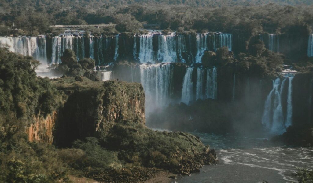 : Majestic view of Raven Cliff Falls cascading down multiple rock ledges surrounded by dense green forest and mist rising from the base