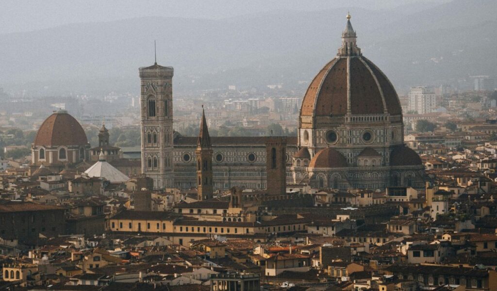 Panoramic view of Florence, Italy, featuring the iconic red-domed Cathedral of Santa Maria del Fiore, Giotto’s Bell Tower, and surrounding historic rooftops.