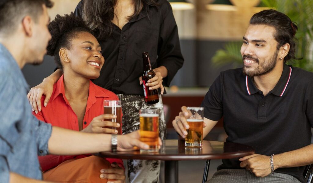 A group of friends sitting around a table, holding glasses of beer and smiling, enjoying drinks and conversation together.