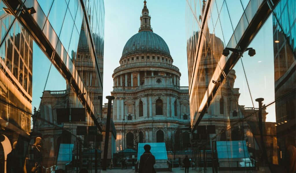 View of St. Paul’s Cathedral in London, England, framed between two modern glass buildings reflecting its grand dome and intricate architecture.
