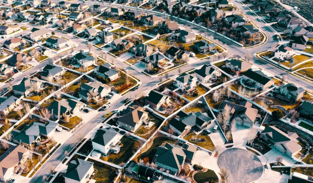 An aerial view of a suburban neighborhood with rows of similar houses, neatly arranged streets, and small yards creating a uniform pattern. 