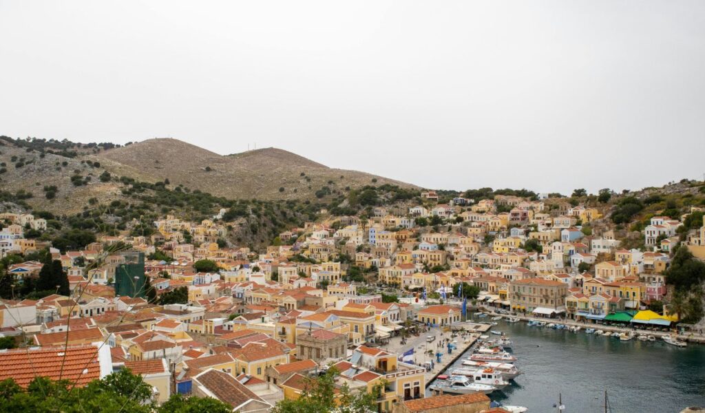 Colorful neoclassical houses of Symi, Greece, climb up the hillside from the harbor, creating a picturesque view against the rocky landscape.