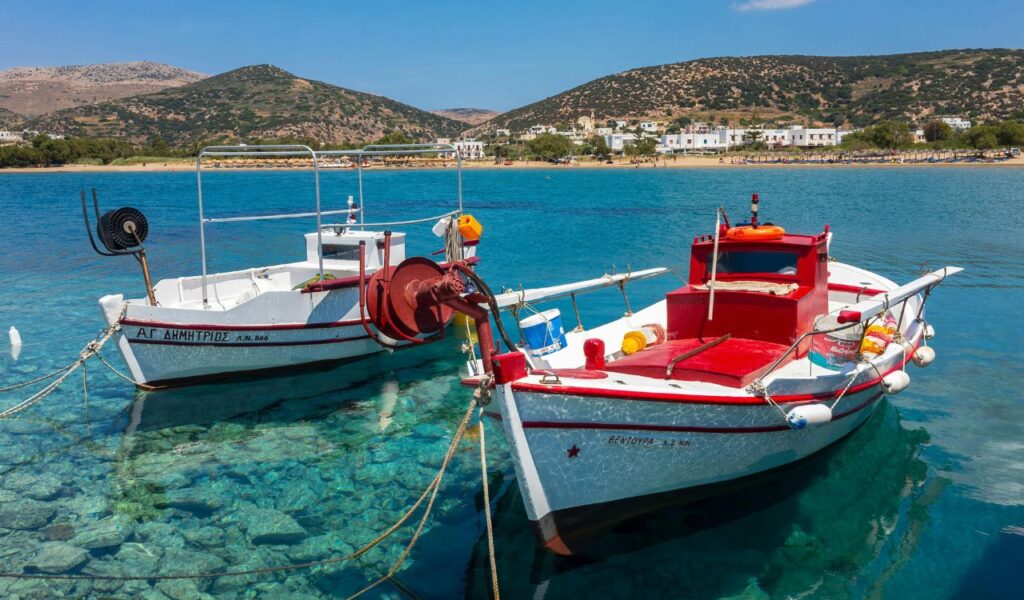 Two traditional Greek fishing boats with red and white paint float on crystal-clear turquoise waters near the shore of Syros island.