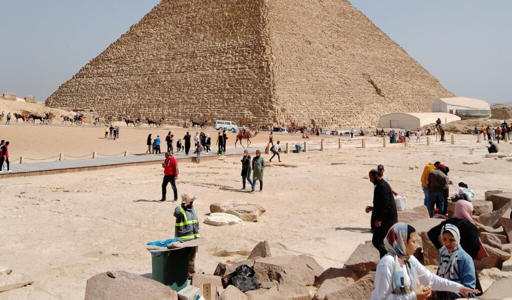 Tourists and local guides near the base of the Great Pyramid of Giza, with camels and visitors exploring the historic site.
