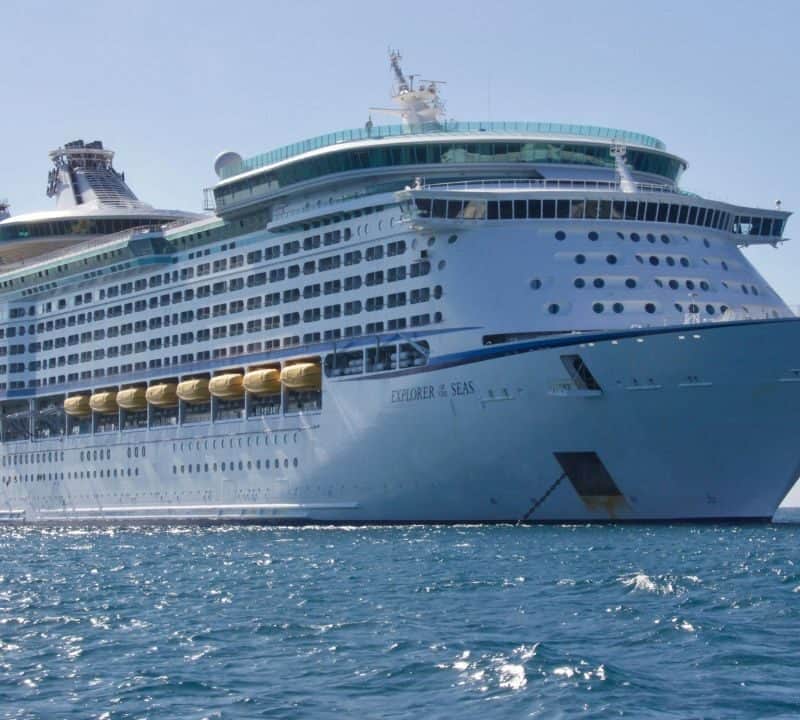 A large white cruise ship named Explorer of the Seas sailing on calm blue waters under a clear sky