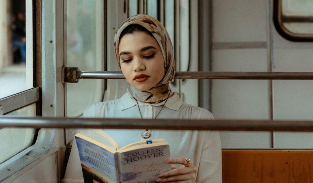 A woman wearing a headscarf reads a book while riding public transportation in Egypt, reflecting a local travel experience.