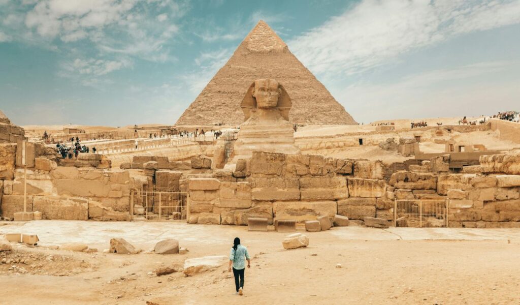A lone traveler walks toward the Sphinx and Great Pyramid of Giza on a quiet day, avoiding the usual tourist crowds.