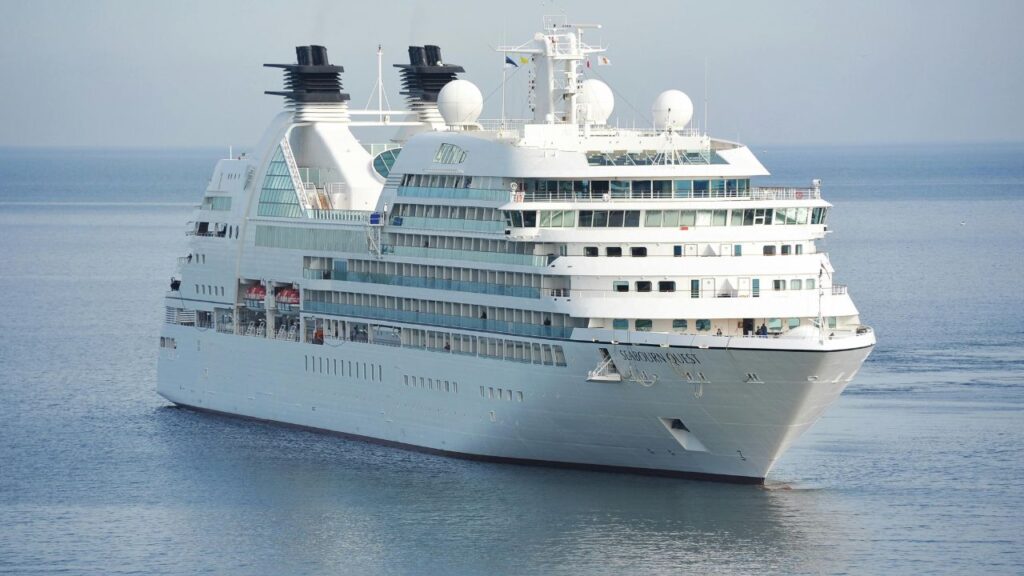 Large white cruise ship named Seabourn Quest sailing on calm blue waters under a clear sky.