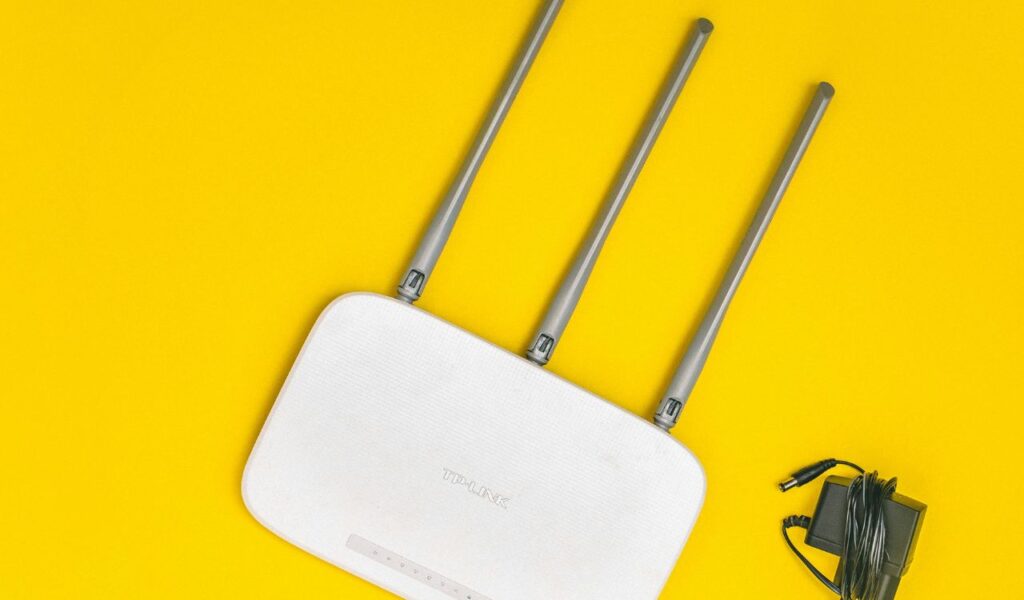 A white TP-Link Wi-Fi router with three antennas and a power adapter placed on a bright yellow background