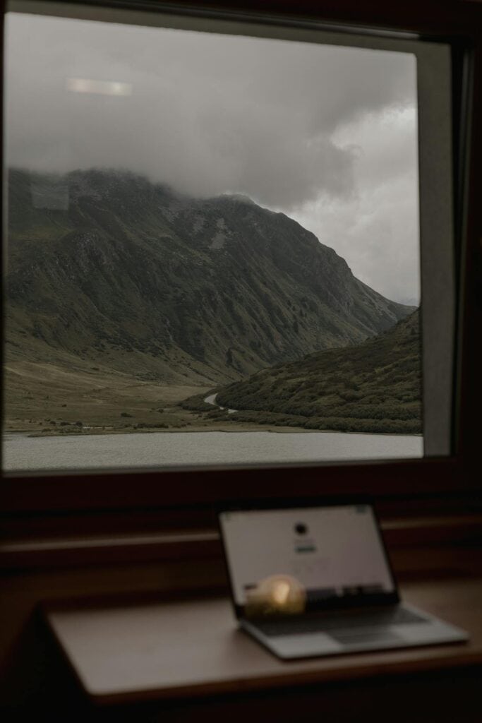 A laptop on a porch overlooking scenic countryside or lakeside.
