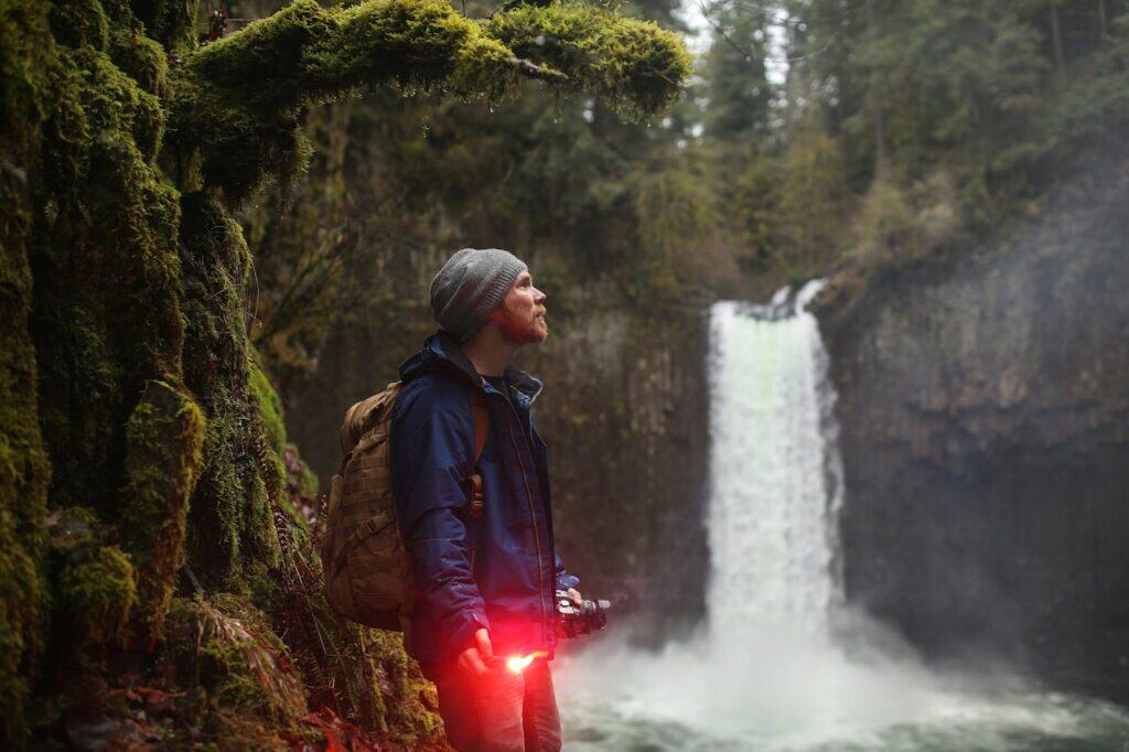 A hiker standing near a misty, hidden waterfall surrounded by dense forest,