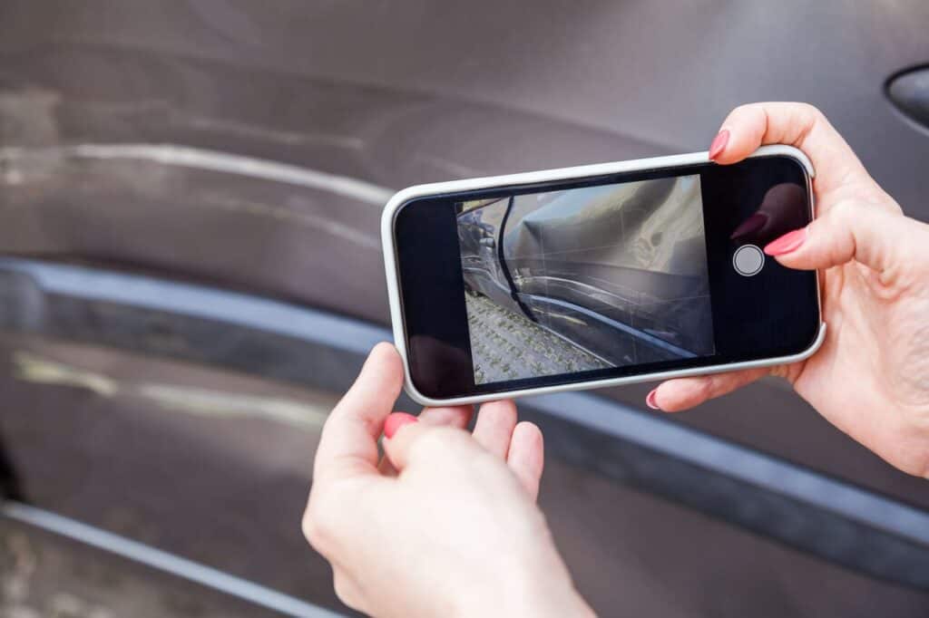 Person photographing scratches on a car with a phone.