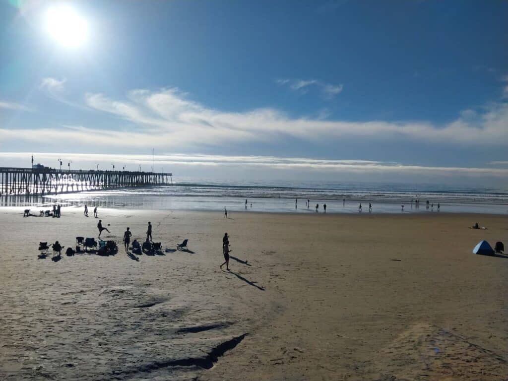 Sunlit California beach with pier, people enjoying coastal views, and clear blue sky - perfect for relaxation and beach activities.