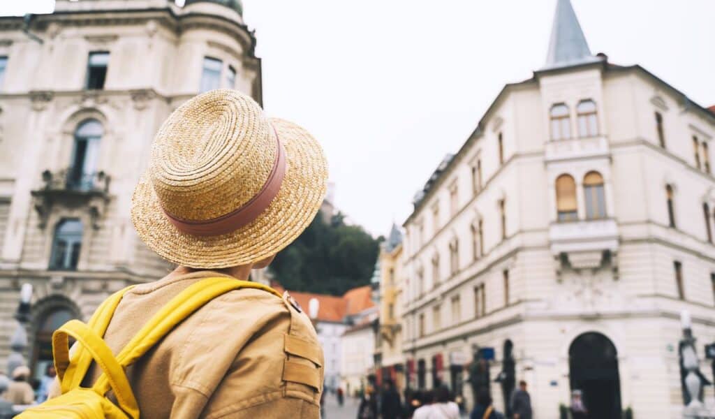 Travel Slovenia, Europe. Young girl with backpack on Triple Bridge in heart of Ljubljana Old Town. Back view of woman tourist on the background of city architecture. Local living in Ljubljana