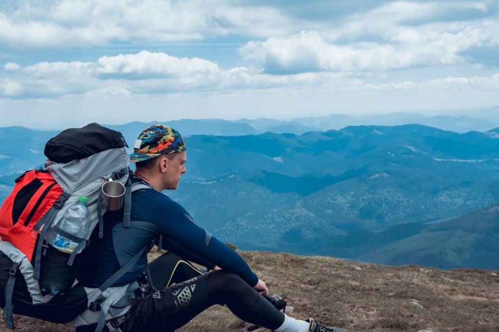 Wide-angle shot of a hiker resting with panoramic foothills or medium-altitude scenery in the background.