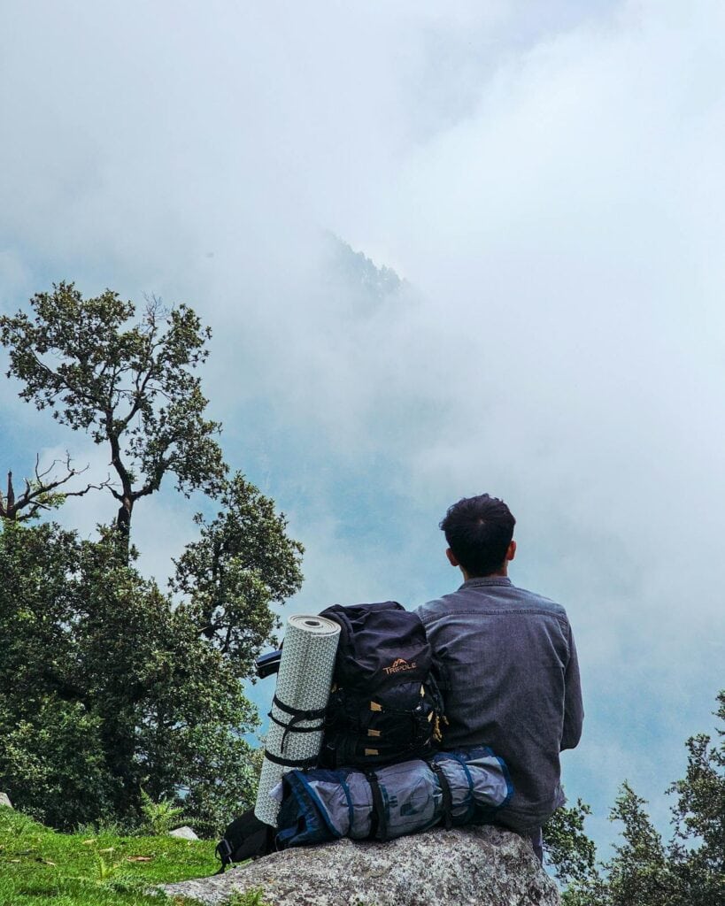 Candid image of a trekker pausing to hydrate, appearing thoughtful or slightly fatigued, with dramatic high-elevation landscape visible.