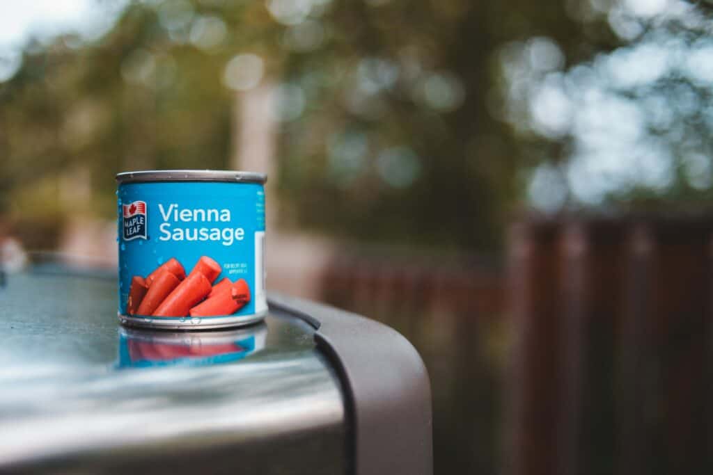 Vienna Sausage canned food on outdoor table with blurred nature background.