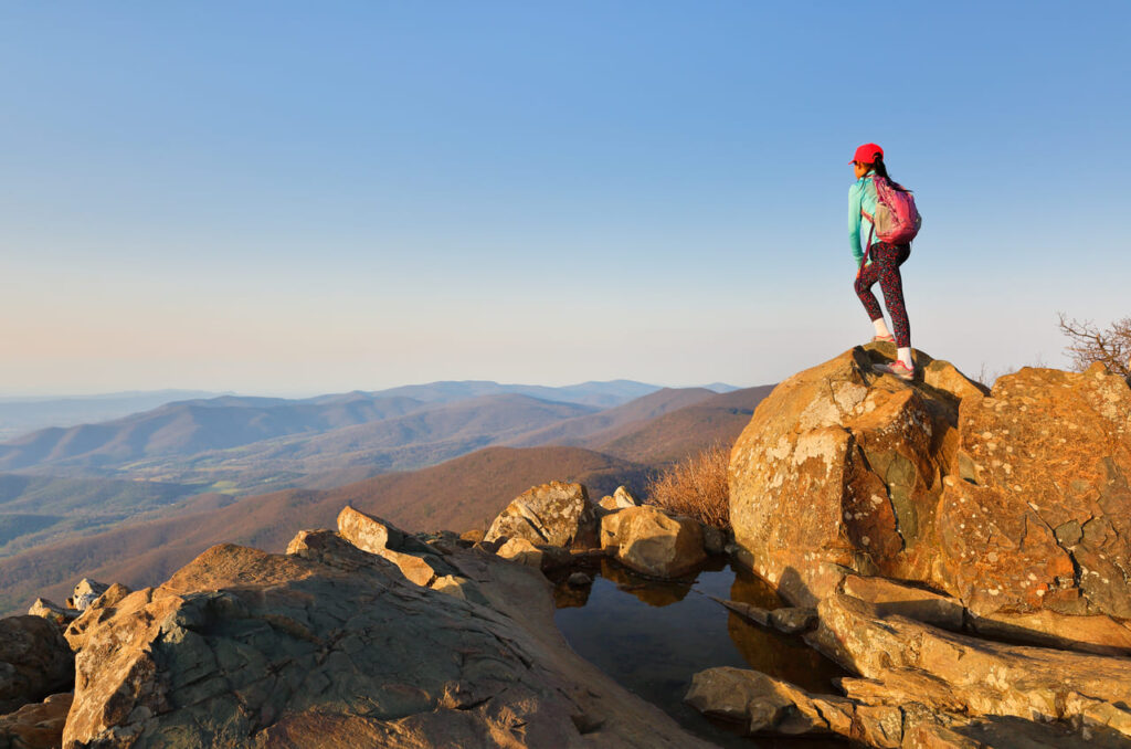 A young hiker standing on the top of Stony Man Summit at Shenandoah National Park at sunset, Virginia, USA. Shenandoah National Park extends along the Blue Ridge Mountains in Virginia USA.