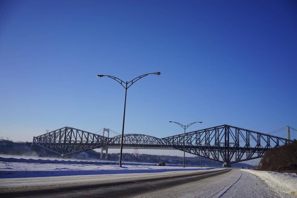Bridge over icy river with clear blue sky, winter daytime, urban infrastructure, scenic landscape.
