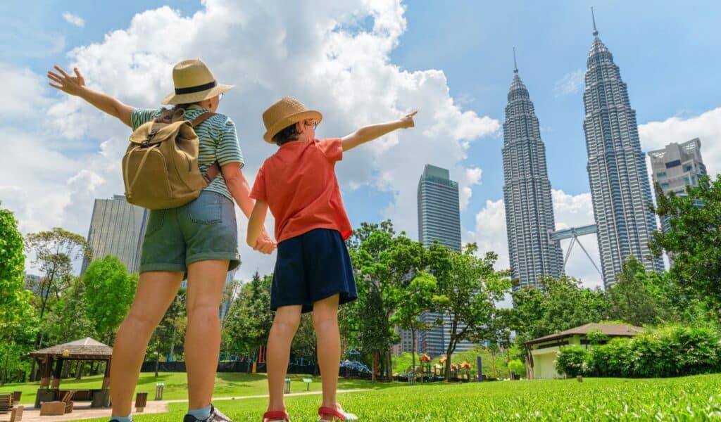 Kuala Lumpur, Malaysia - 2 April, 2025 Female tourist and her son enjoying wonderful cityscape in Kuala Lumpur, Malaysia. Woman and little boy with raised arms at a city park among skyscrapers