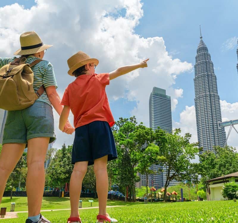 Kuala Lumpur, Malaysia - 2 April, 2025 Female tourist and her son enjoying wonderful cityscape in Kuala Lumpur, Malaysia. Woman and little boy with raised arms at a city park among skyscrapers