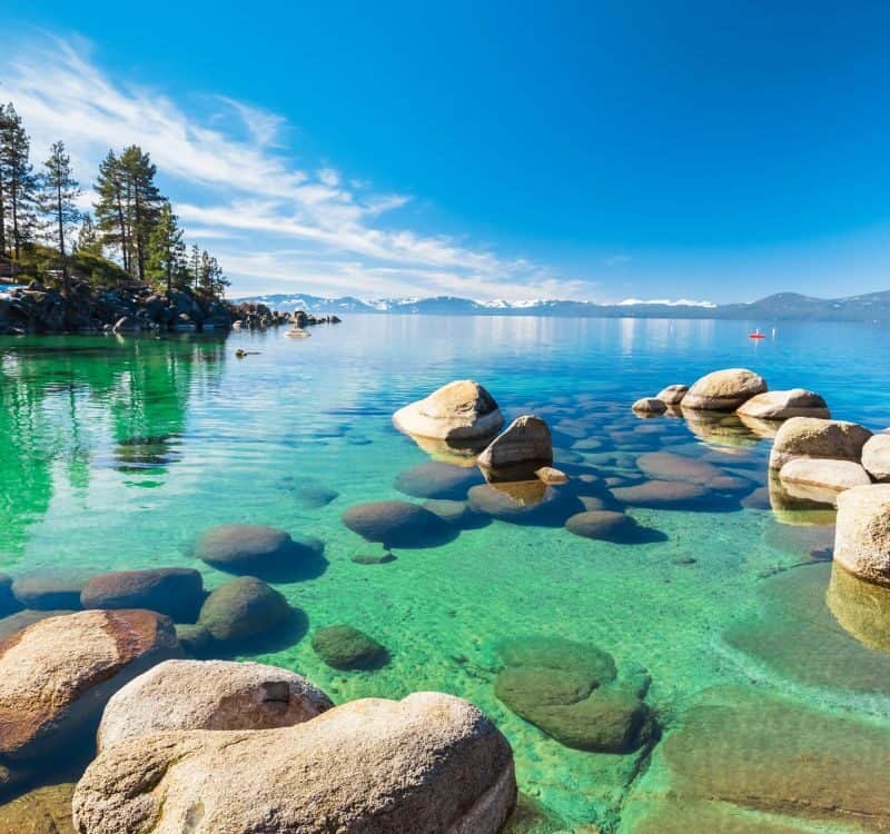 Lake Tahoe rocky shoreline in sunny day, beach with blue sky over clear transparent water