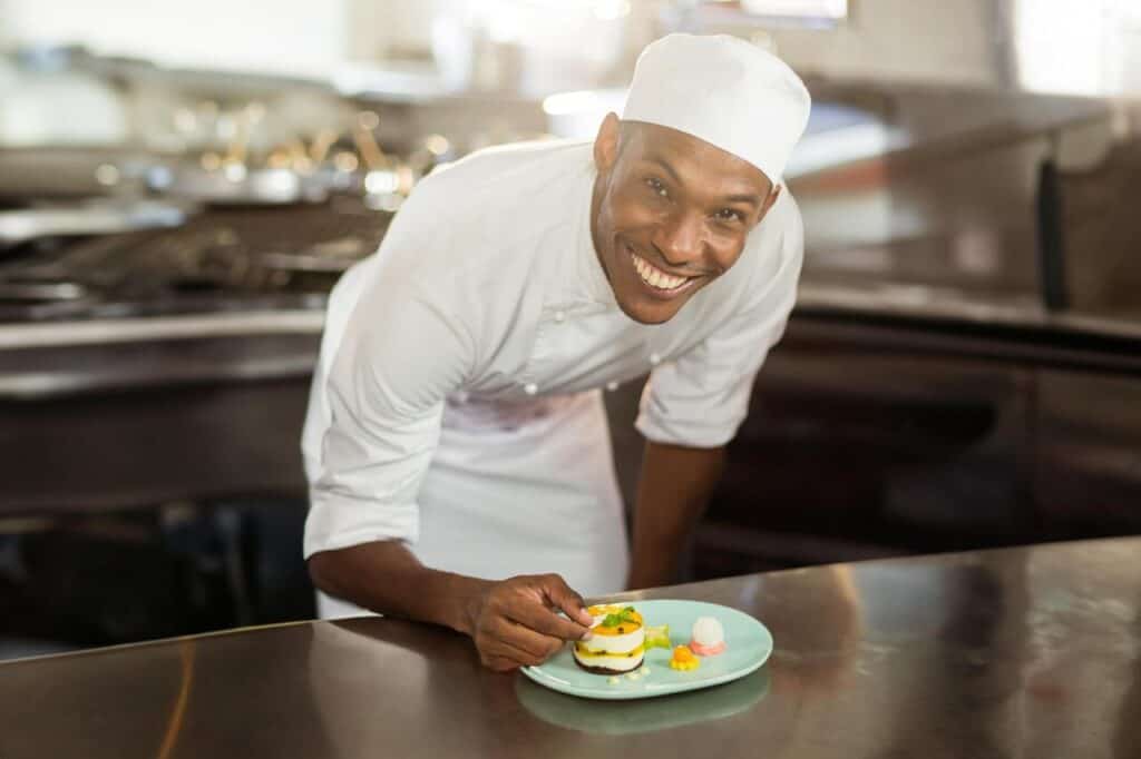 Mid adult African American male chef plating layered dessert on green plate in commercial kitchen.