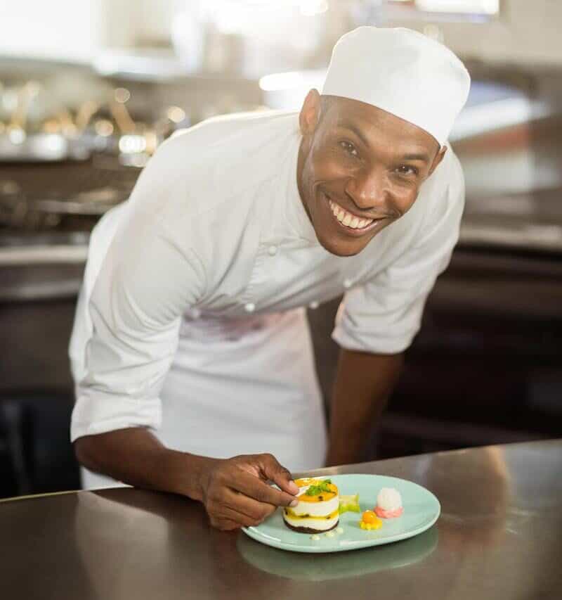 Mid adult African American male chef plating layered dessert on green plate in commercial kitchen.