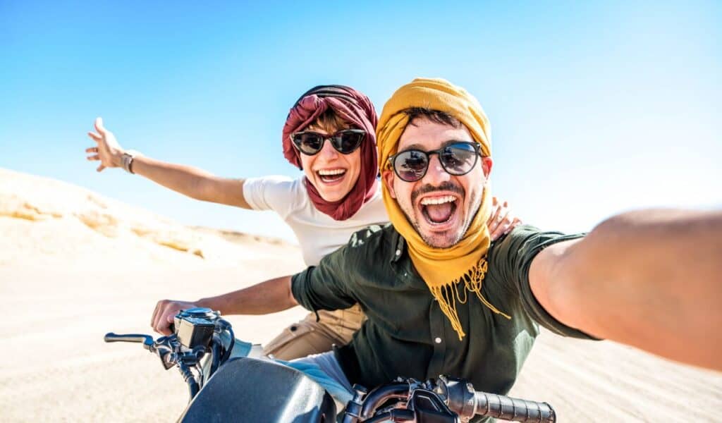 Young couple on a off road adventure excursion outside - Joyful tourists taking selfie with smart mobile phone in the desert