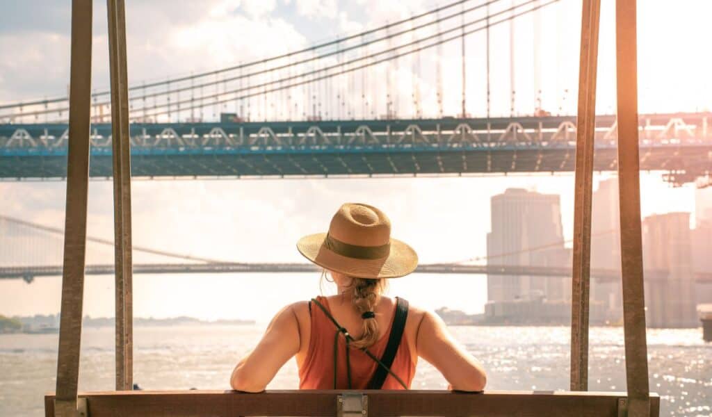 Young tourist woman on the Brooklyn Bridge and Manhattan Bridge. New York city girl walking in summer vacation USA travel lifestyle. Tourism in the USA NYC skyline in back.