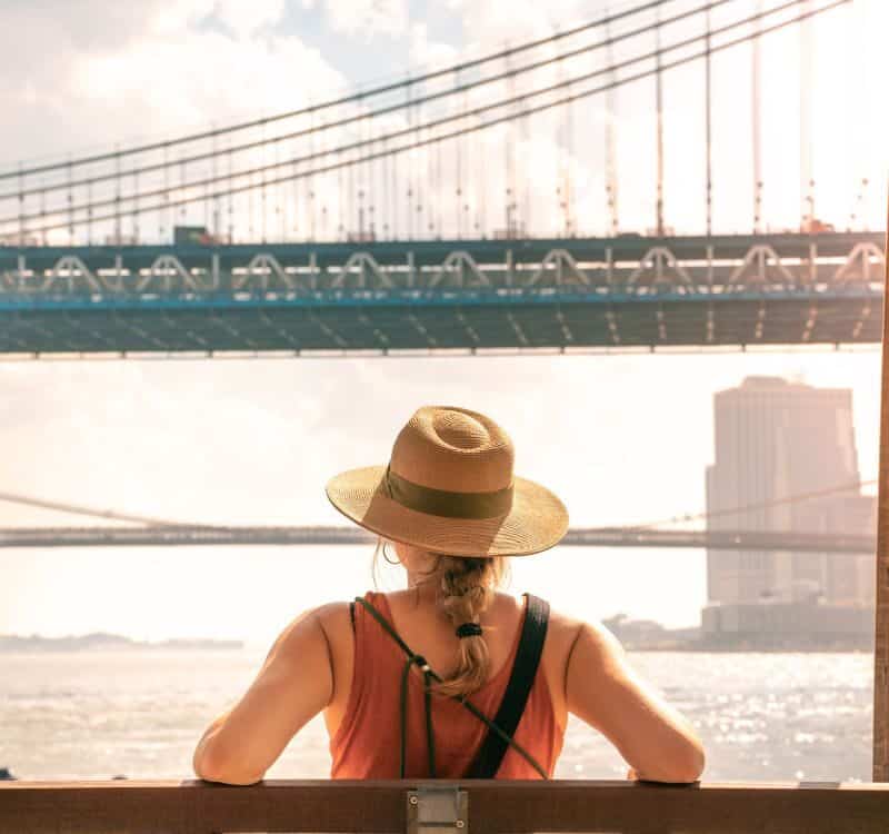 Young tourist woman on the Brooklyn Bridge and Manhattan Bridge. New York city girl walking in summer vacation USA travel lifestyle. Tourism in the USA NYC skyline in back.