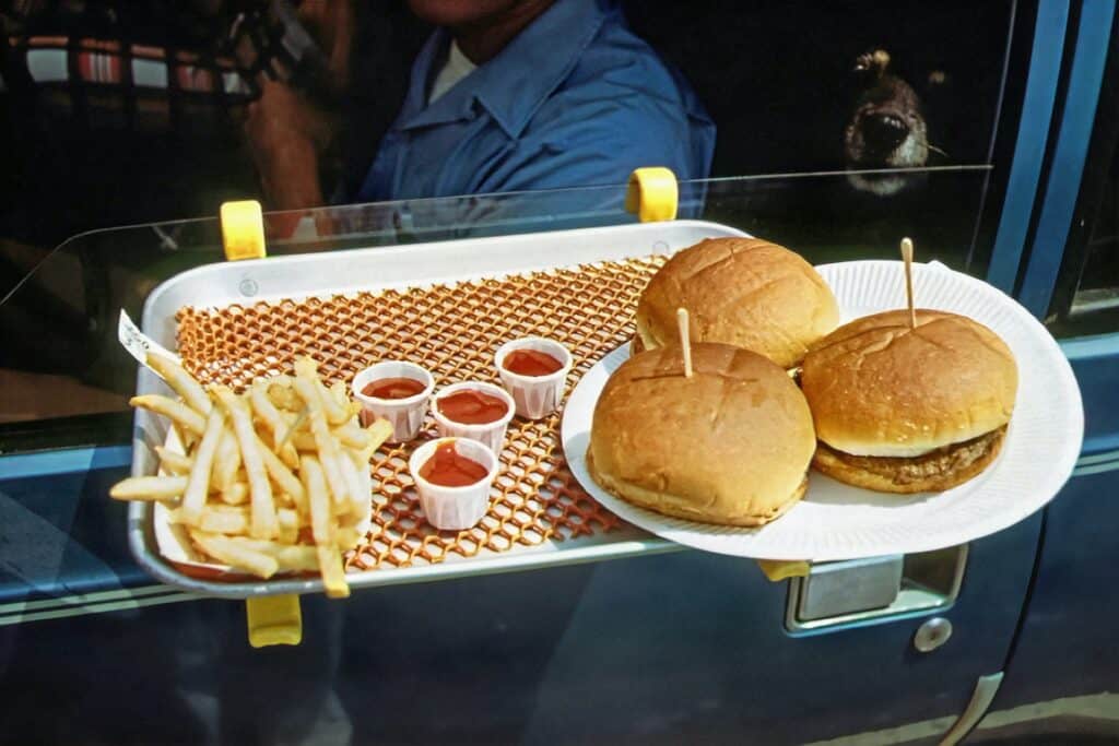 close-up of burgers, fries, and soft drinks on plastic trays