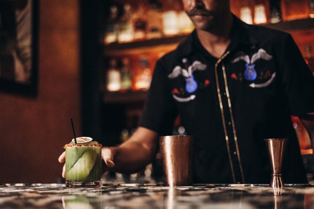 Bartender serving a zero-proof cocktail in a dim, art-deco style setting.