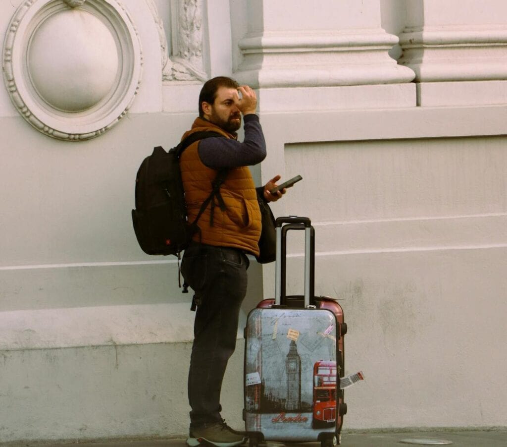 Traveler standing outside with luggage, looking confused.