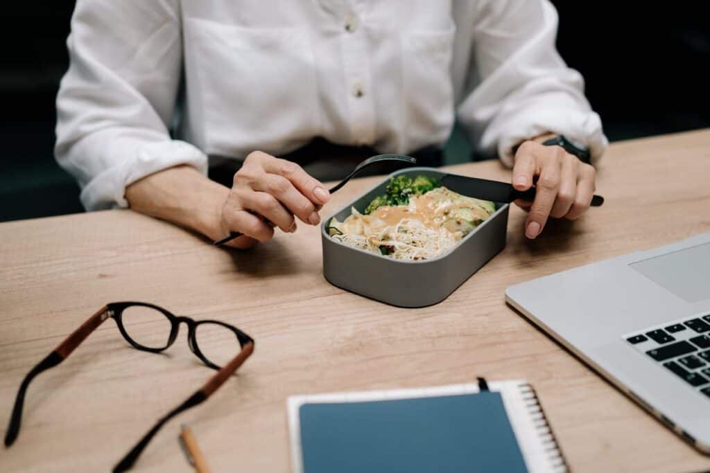 A packed lunch in a reusable container next to a laptop on a work desk.