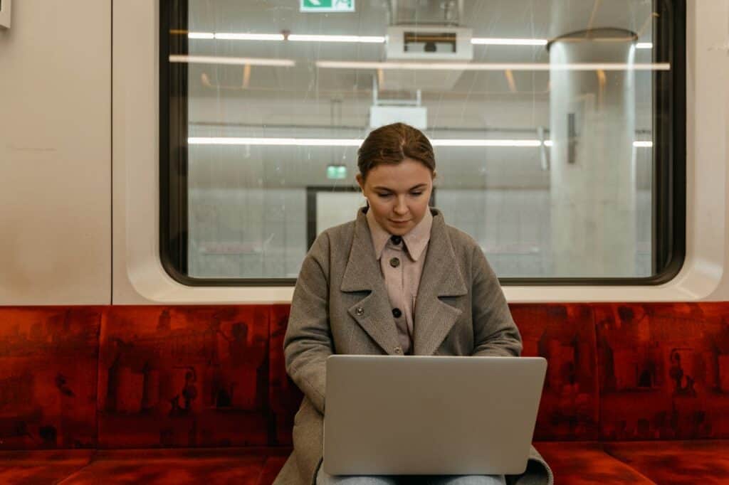 A Woman in Gray Coat Using a Laptop inside a Tram