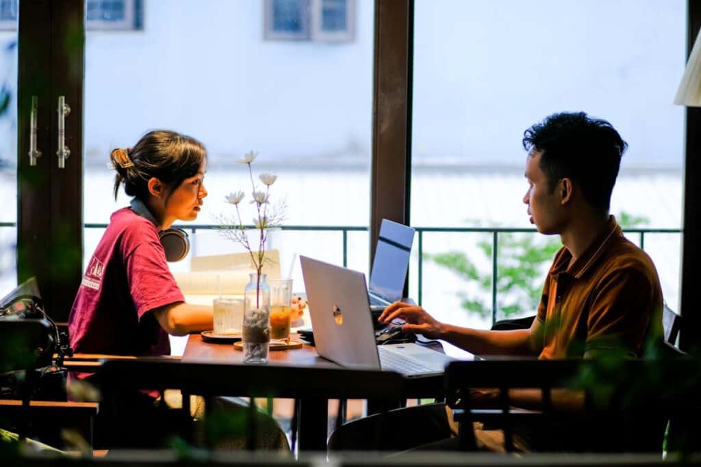 Friends sitting in a café-bar hybrid space with laptops and drinks.